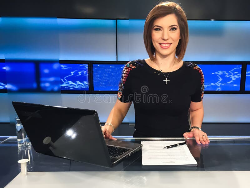 Professional news reporter sitting at desk with laptop and documents, reporting on breaking international news and latest world news updates in modern television studio